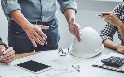 Contractor and developer reviewing building plans with hard hat and calculator